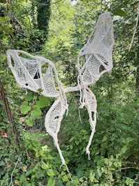 a white crocheted butterfly hanging from a tree in the woods